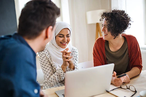 Frau mit Kopftuch sitzt zusammen mit einer Frau und einem Mann vor einem Laptop